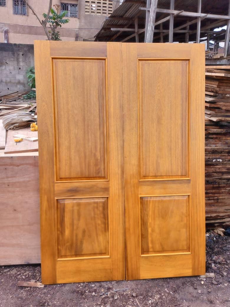 Porte double en bois clair à deux panneaux, photographiée dans la cour de l'atelier DKBOIS